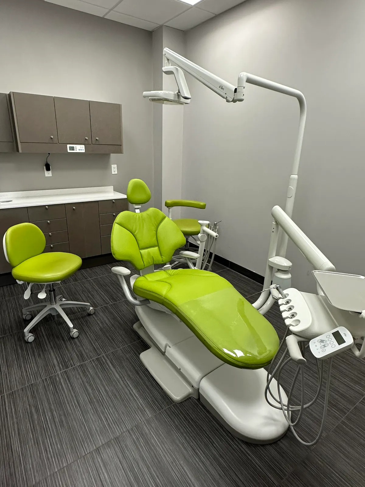 LIV treatment room with a lime-green dental chair, matching stools and grey cabinetry