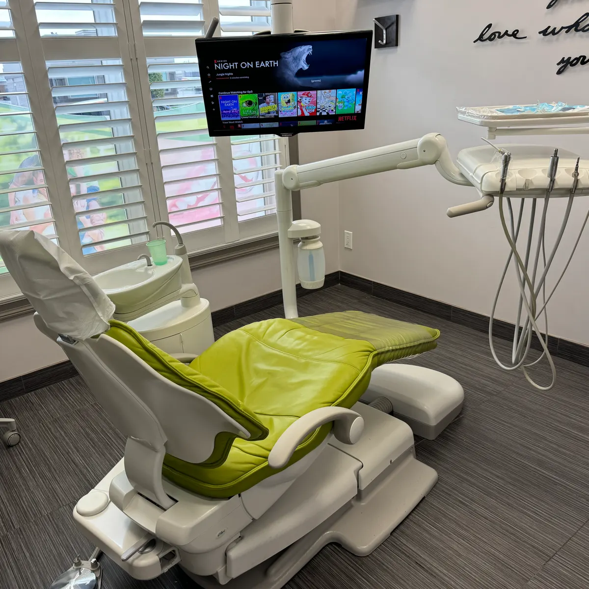 LIV treatment room with a lime-green dental chair beside a shuttered window and a monitor on an arm