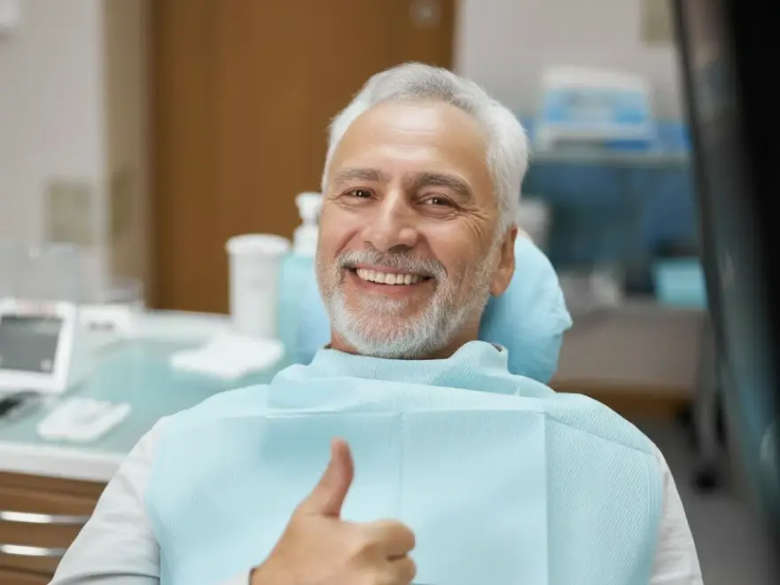 A smiling older man giving a thumbs-up in the dental chair