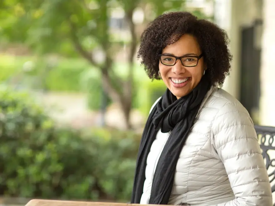 A smiling woman with glasses and a scarf outdoors