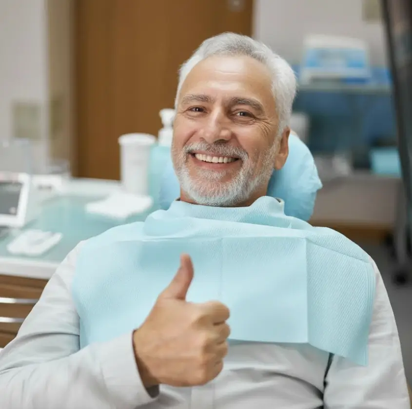 A smiling senior man giving a thumbs-up in the dental chair