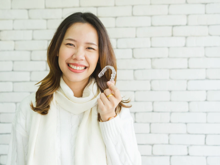 A smiling woman holding a clear aligner