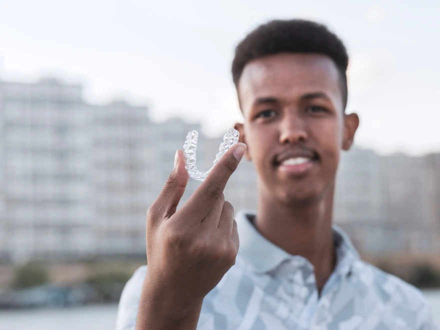 A young man holding up a clear aligner