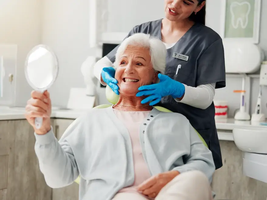 An older patient holding a hand mirror while a team member checks her smile