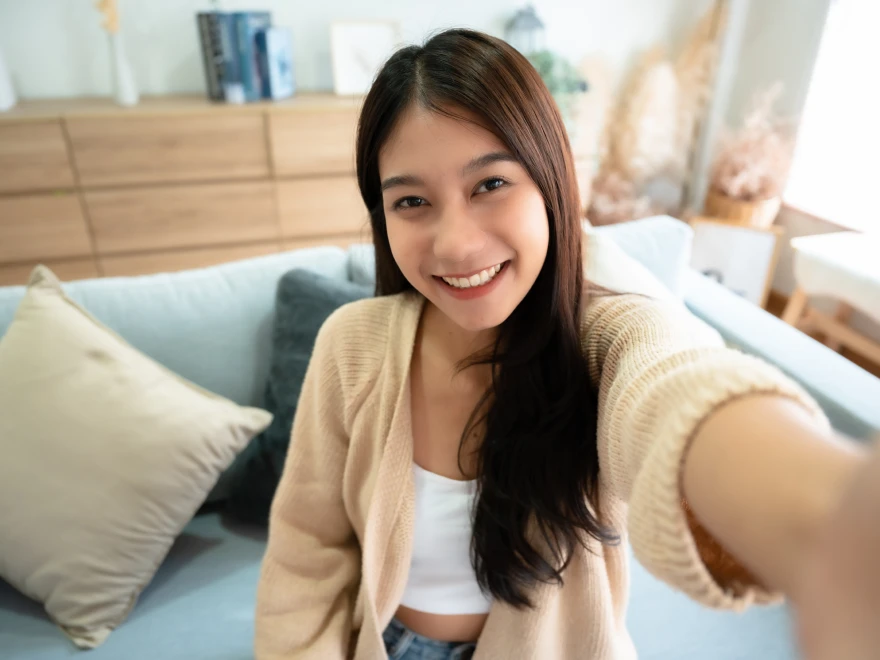 A smiling young woman taking a selfie on a sofa