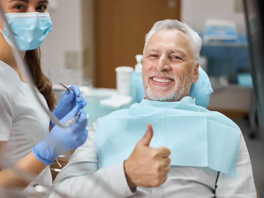 A smiling older man giving a thumbs up in the dental chair