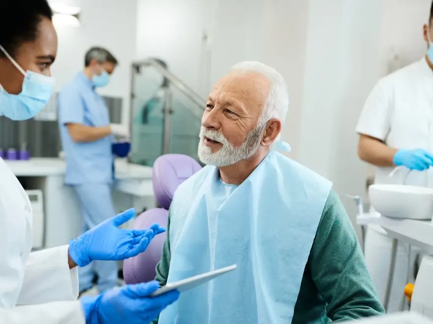 An older man in the dental chair with team members nearby