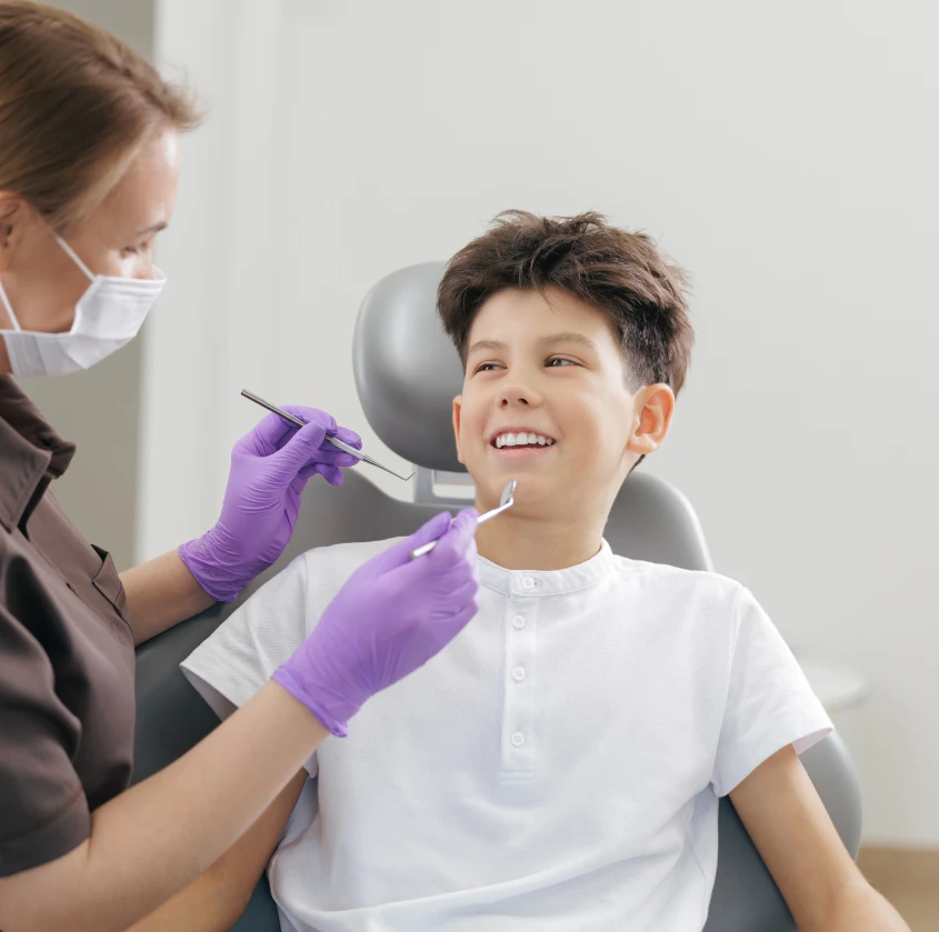 A teen patient in the dental chair while a hygienist works on his teeth