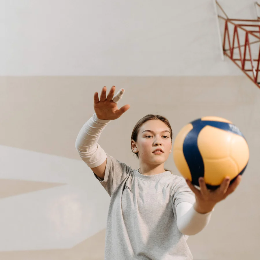 A teenage volleyball player reaching up to serve a ball