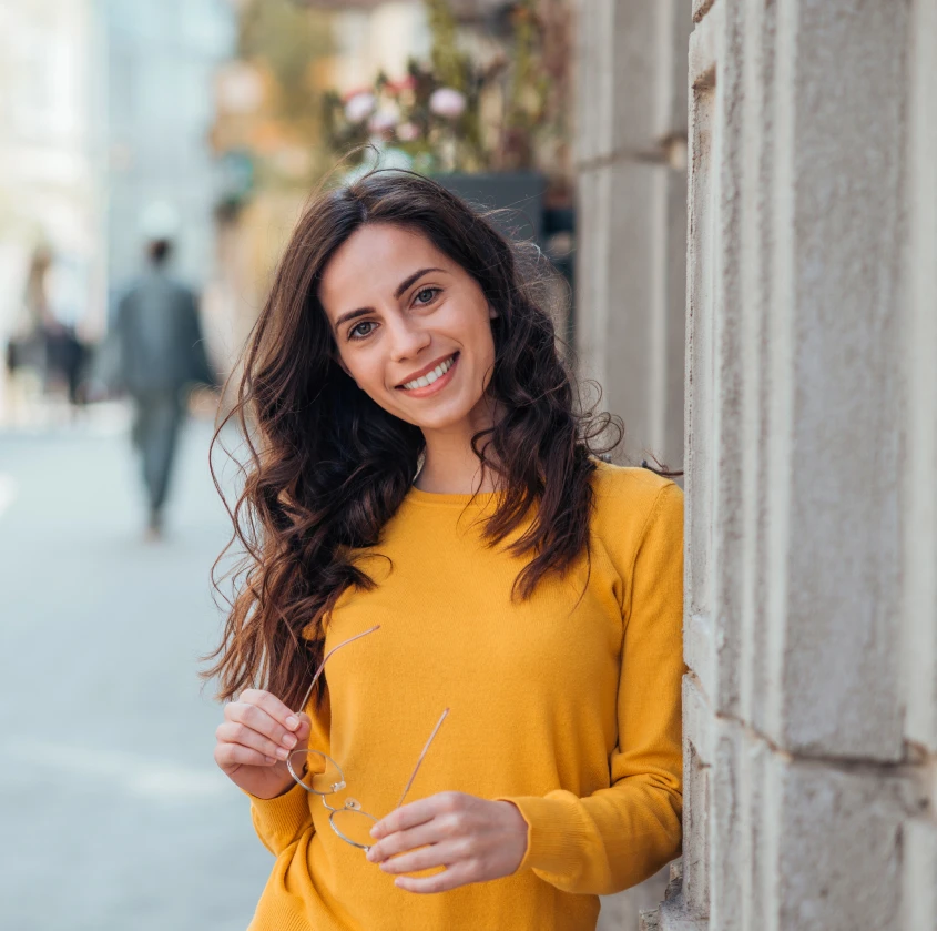 A smiling woman in a yellow sweater outdoors